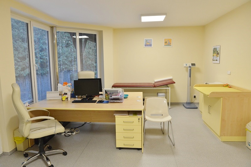 Světlá ordinace s pracovním stolem, lehátkem a přebalovacím pultem